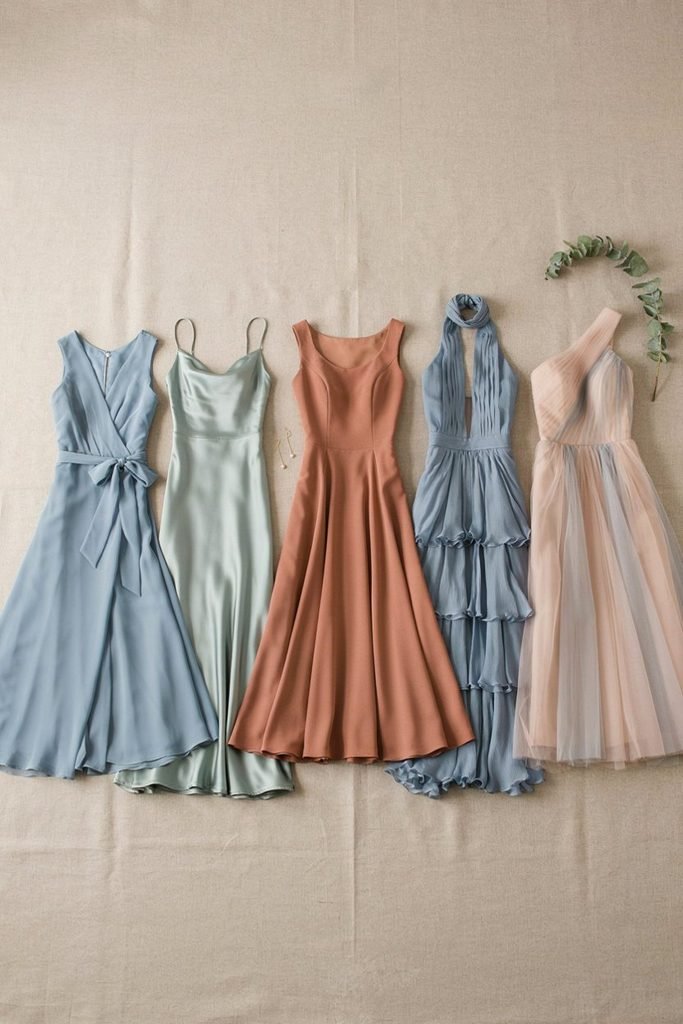 Five mismatched bridesmaid dresses in coordinating dusty blue, sage, and terracotta tones laid out together