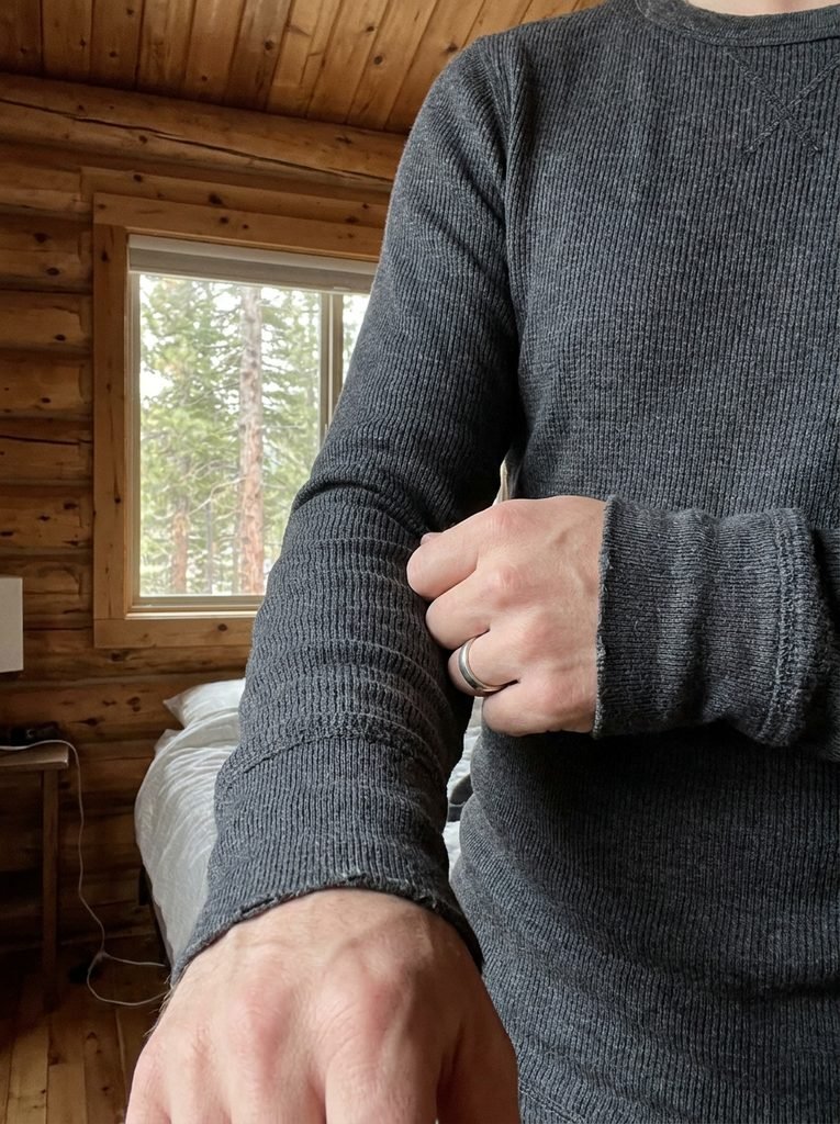 Close-up of a person putting on a merino wool base layer in a cabin bedroom