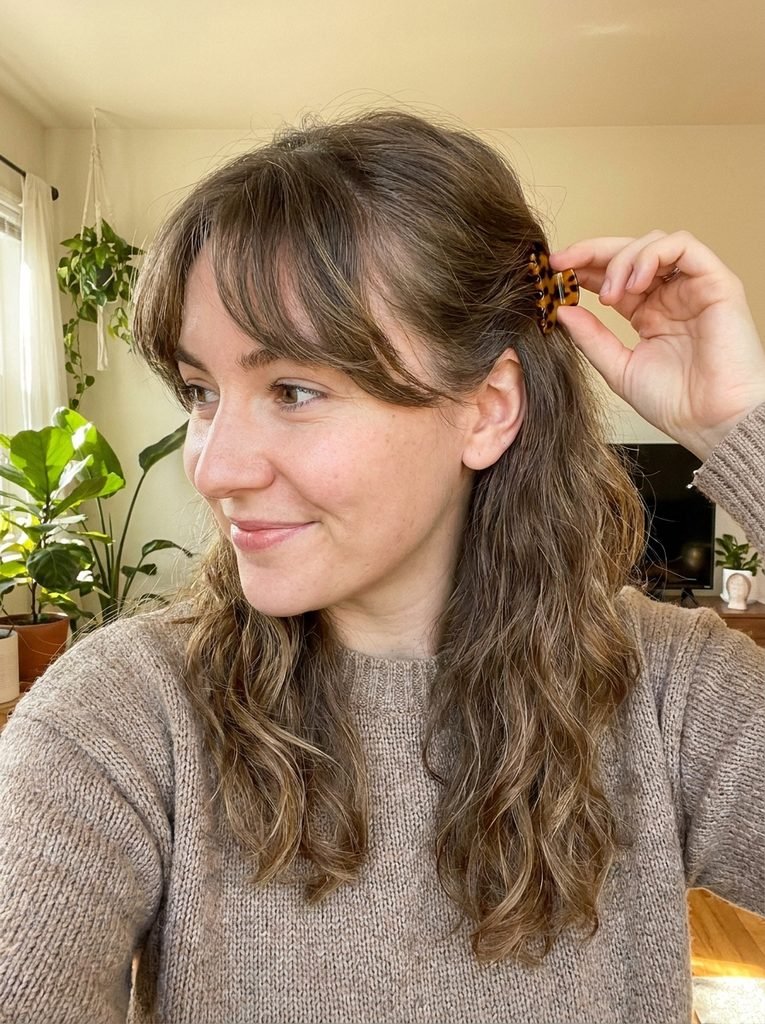 Woman tucking grown-out curtain bangs behind her ears with a small clip