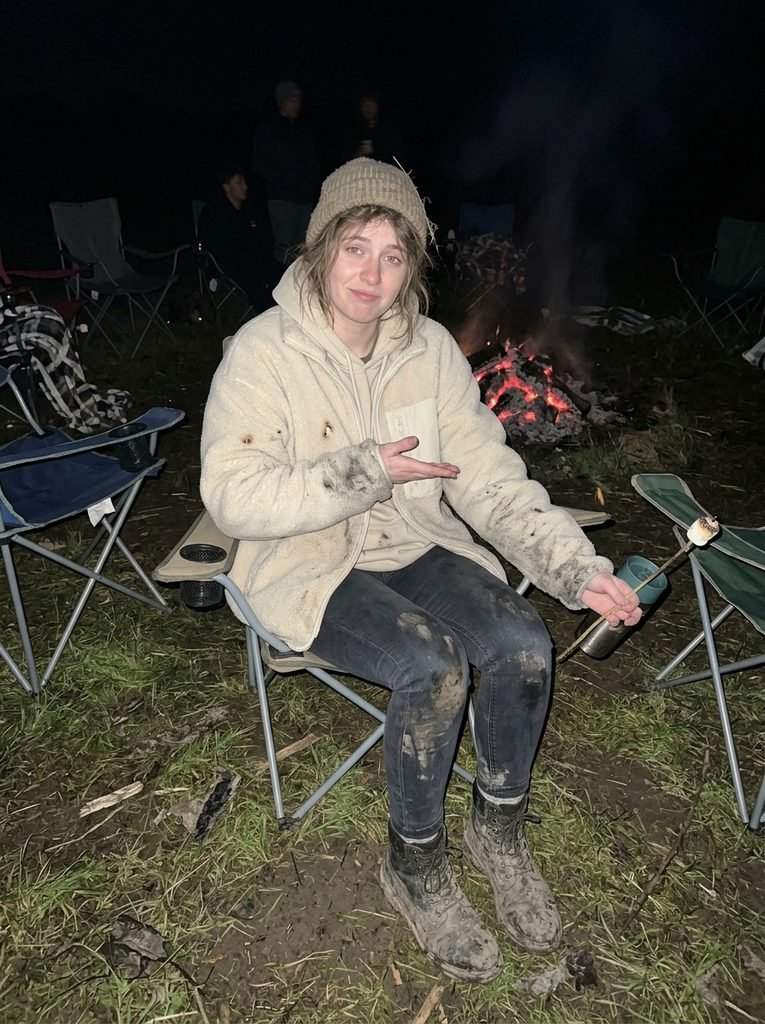 Crowd standing on muddy grass beside a bonfire on a cold evening