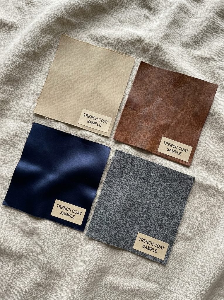 Fabric samples of gabardine, leather, satin, and wool blend used for trench coats laid out on linen