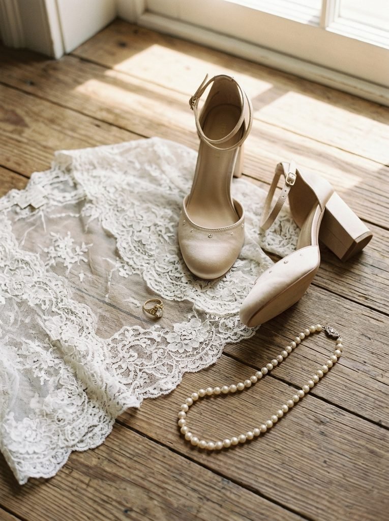 Champagne block-heel shoes, pearl necklace, antique ring, and lace bolero on a wooden floor