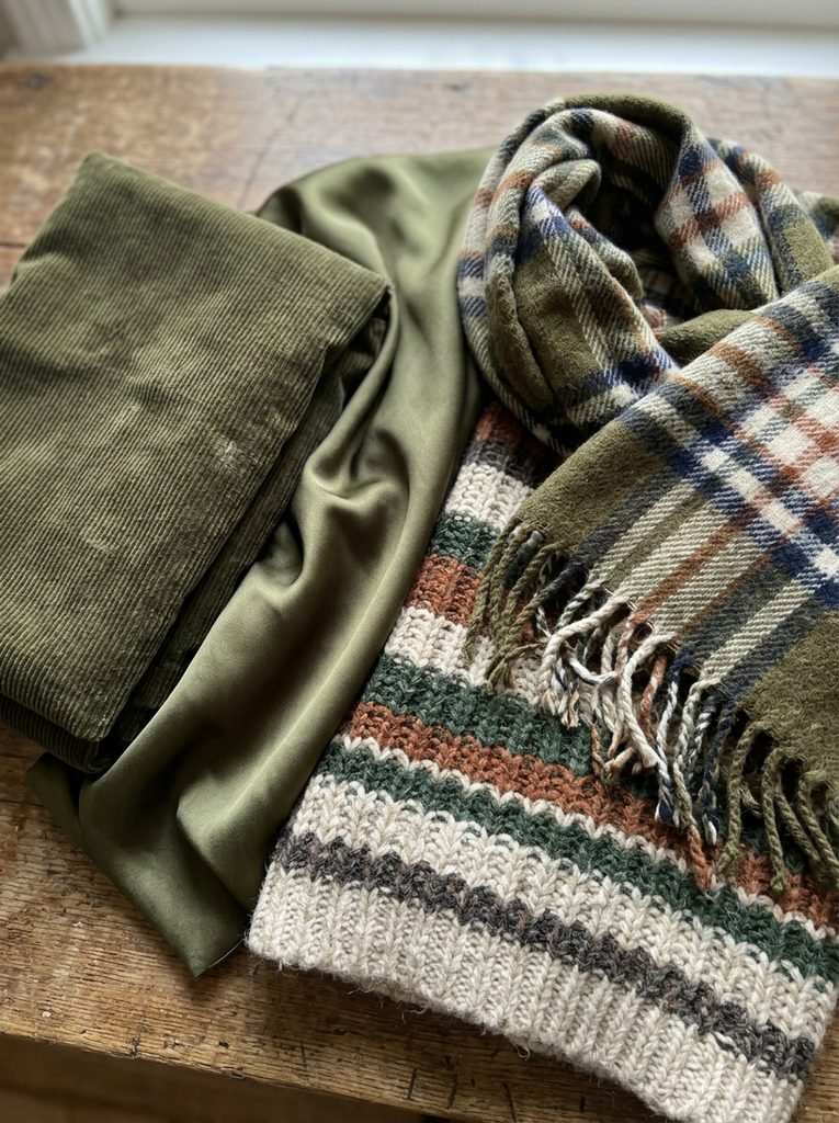 Olive corduroy, olive satin, striped knit, and plaid scarf laid together to show texture and pattern pairings
