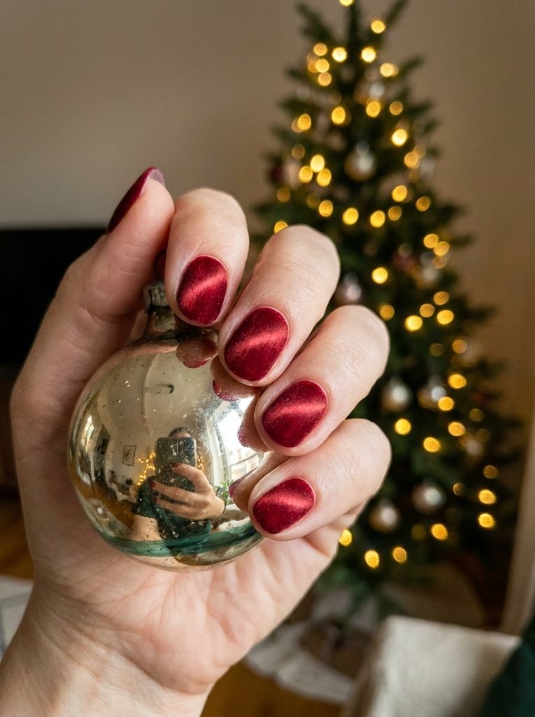 Red velvet cat-eye nails holding a Christmas ornament by string lights