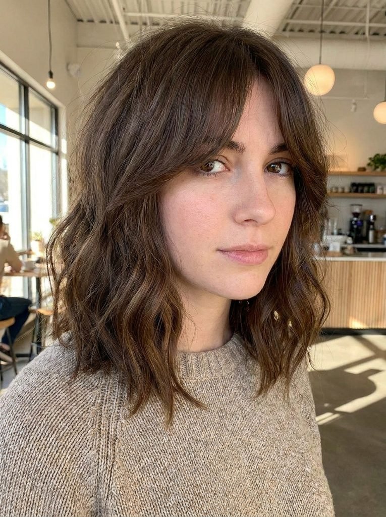 Collarbone lob haircut with center-parted curtain bangs framing the face