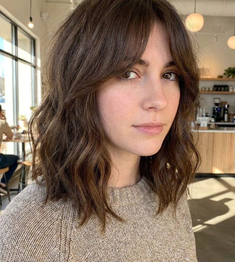Collarbone lob haircut with center-parted curtain bangs framing the face