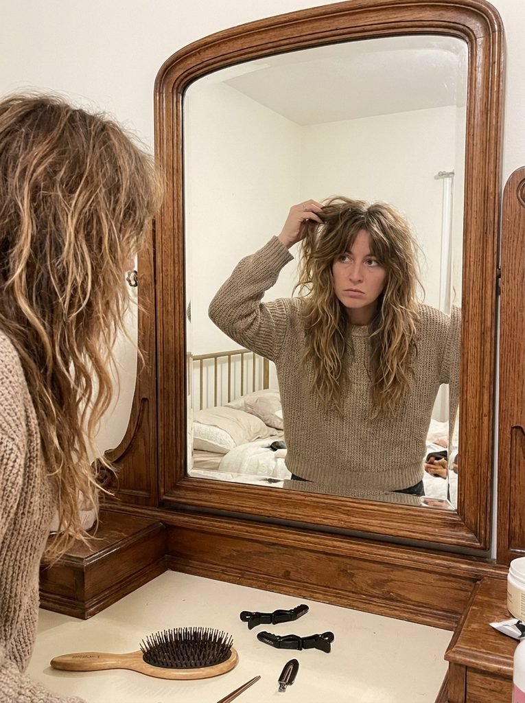 Woman checking a grown-out shag haircut with softened long layers in a home mirror
